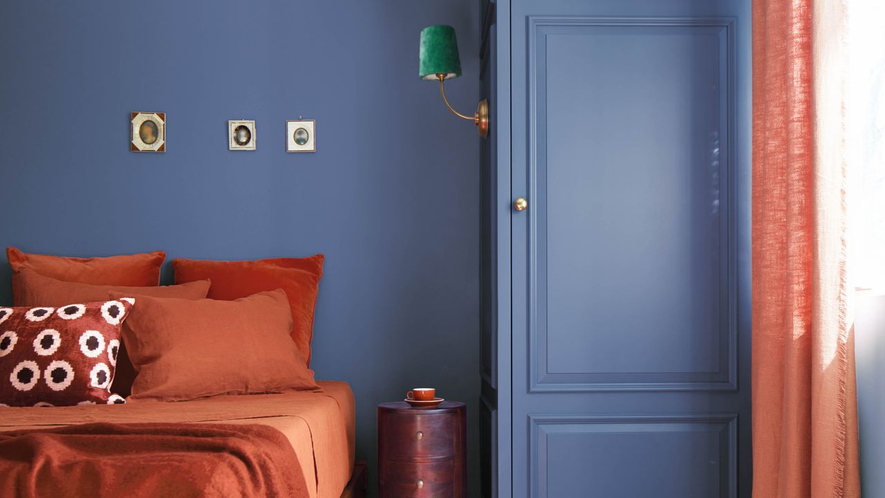 Dark blue bedroom with rust bed covers and green wall lamp