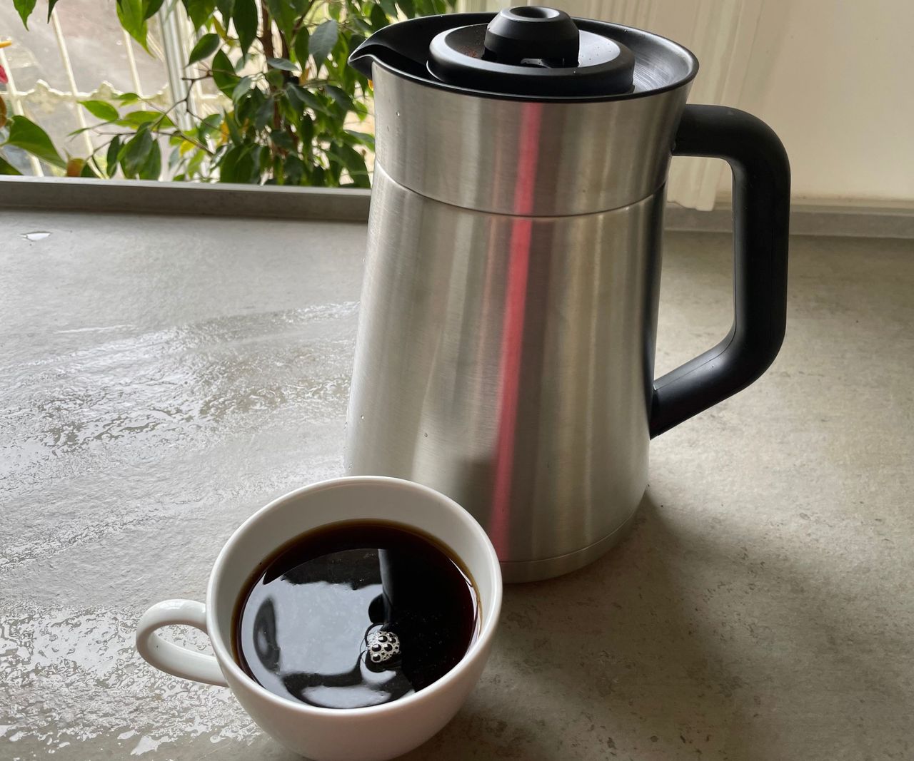 OXO 9 cup coffee maker on a grey countertop with a small white cup of black coffee.