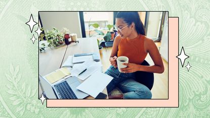 A young woman holds a cup of coffee while sitting at a desk and going through her taxes.