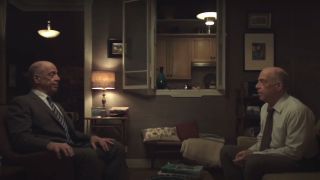 J.K. Simmons sitting across from J.K. Simmons in a living room in Counterpart.