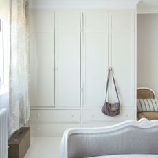 White bedroom with white fitted wardrobes and a handbag hanging from the handle