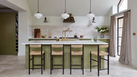 Pink tiled kitchen with green island, rattan bar stools with black frames, and green cabinetry. To the right is a large crittal door with pink and white striped curtains.