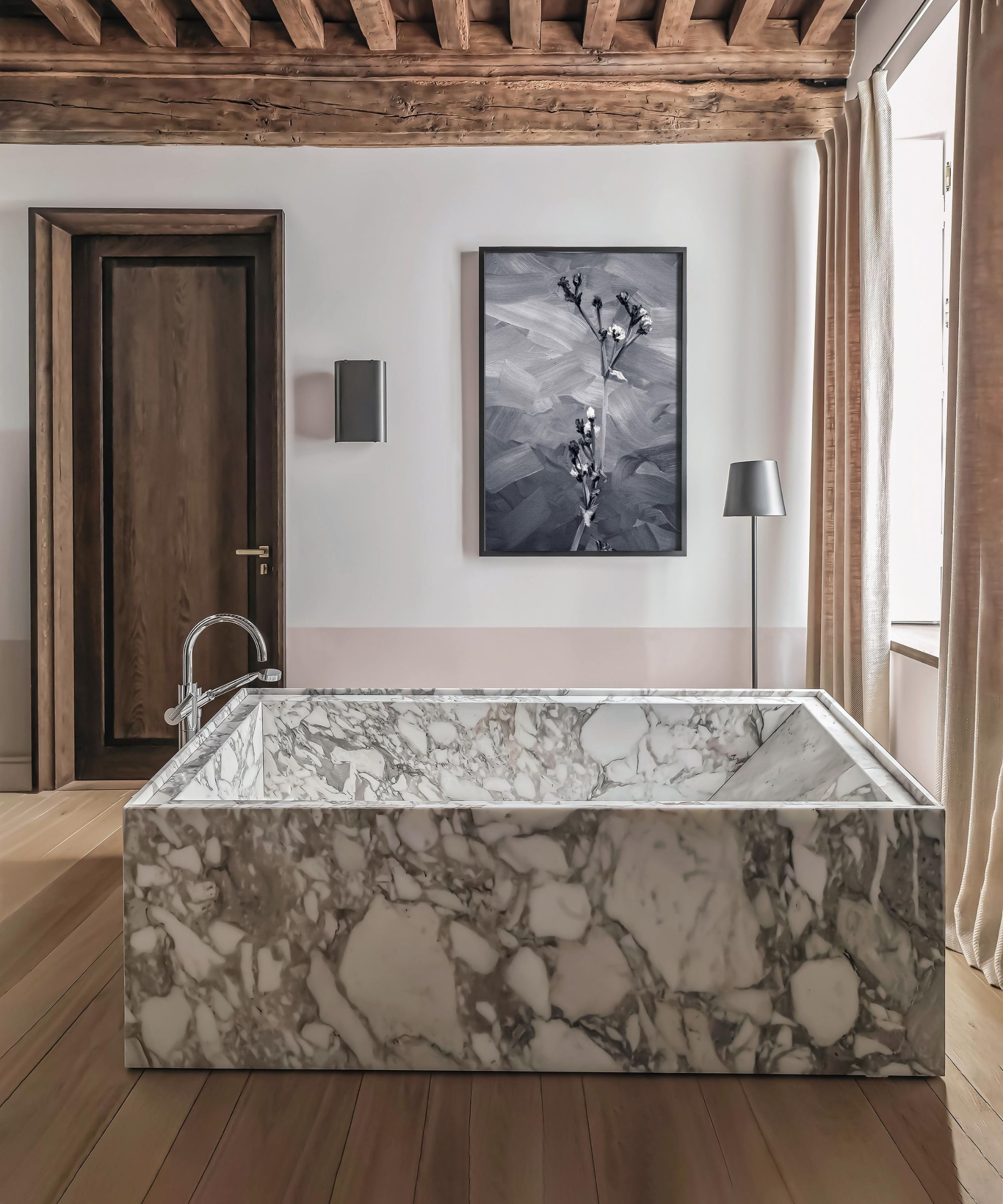 a large bathroom in a townhouse in France with original ceiling beams, wooden floor and door with a huge entirely marble bathtub in the middle of the room