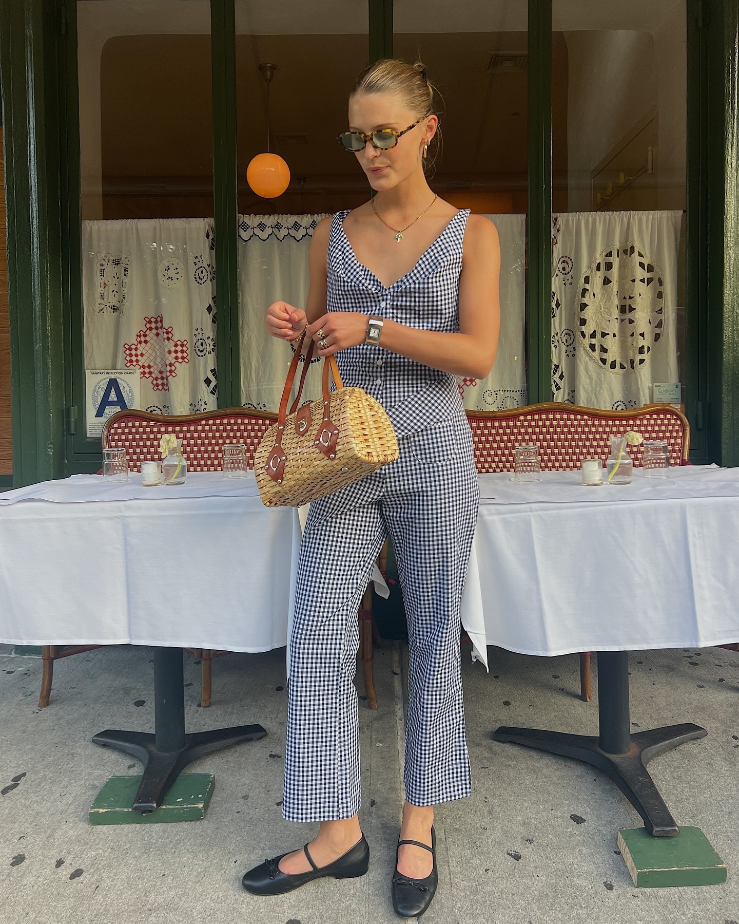 A woman wearing a peak top and pants, black ballet flat and wicker bag.