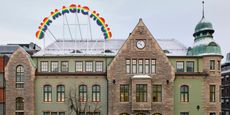 The brick and copper facade of a historic building is covered in a thin layer of snow at dusk and decorated with a rainbow-hued sign that reads "OUR MAGIC HOUR"