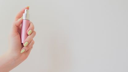 young woman holding a bottle of perfume in hand. metal bottle with spray on a white. cosmetology beauty pattern; refillable perfume atomizer in a woman's hand and a white background