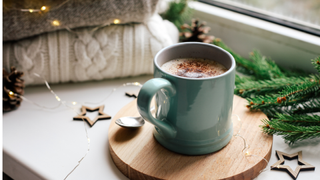 Window sill with a blue mug of hot chocolate, Christmas tree branch, star decorations and wooly jumpers folded up