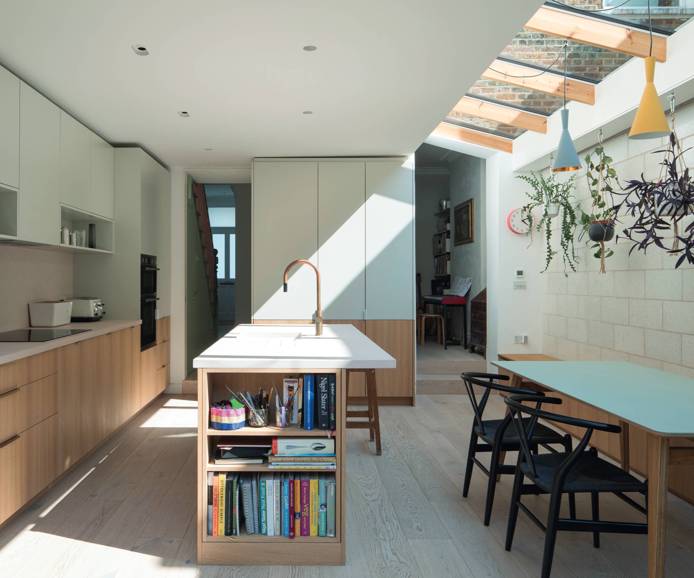 An extended terrace house kitchen with modern timber units, kitchen island and dining bench, with roof glazing bringing in natural light