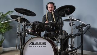 Man in black hoodie playing an Alesis electronic drum set