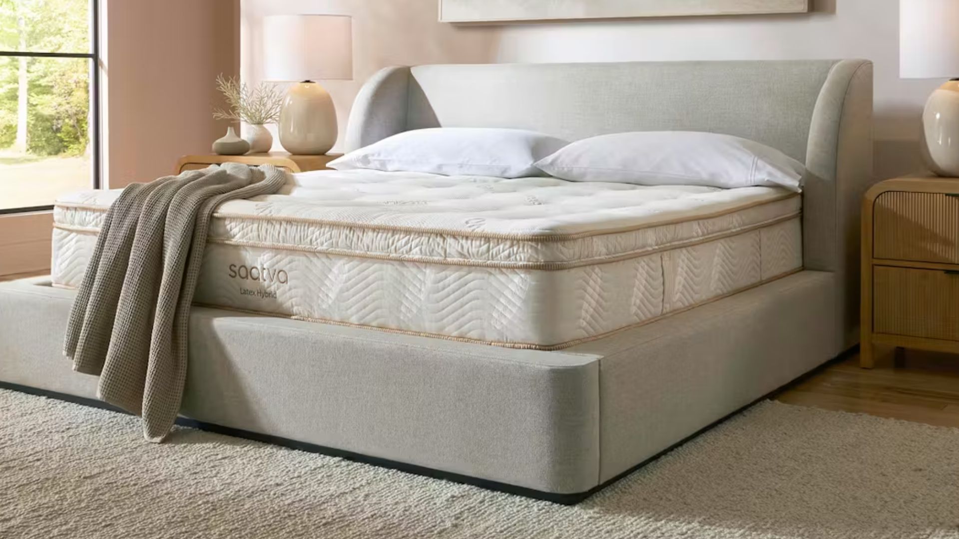 The image shows a cream mattress with gold piping placed on a beige bed frame, which is set within a neutrally decorated bedroom