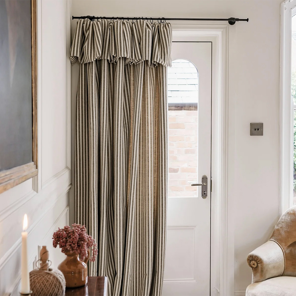 Striped green and cream door curtain with a frill on a black curtain pole half pulled across a white front door