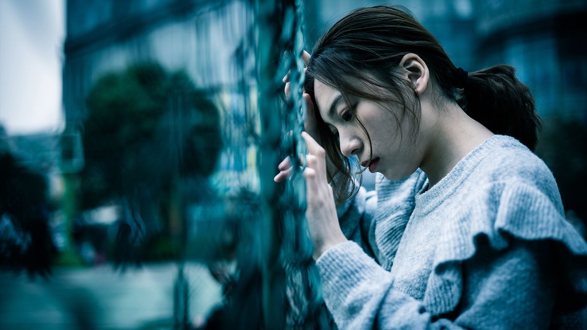 Depressed teenage girl stands against a wall in angst.