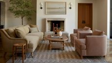 Cream sofa and dusty pink armchairs encircling a wooden coffee table on a beige rug against cream walls.