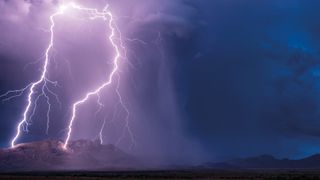 Intense lightning strikes illuminating a mountainous landscape under a stormy sky