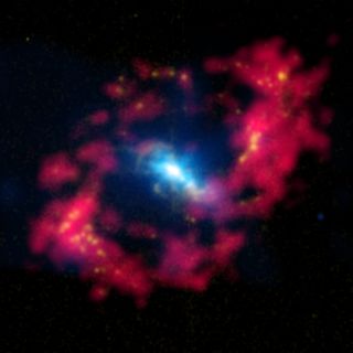 a bright blue central glob shines engulfed in blue gasses. Around it in a tall oval shape is a ring of red gasses.