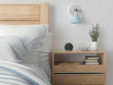 A black Amazon Echo smart speaker on a wooden nightstand next to a bed