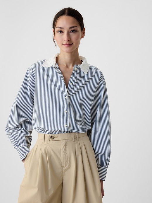 a model wears a blue and white striped button-down shirt with beige trousers