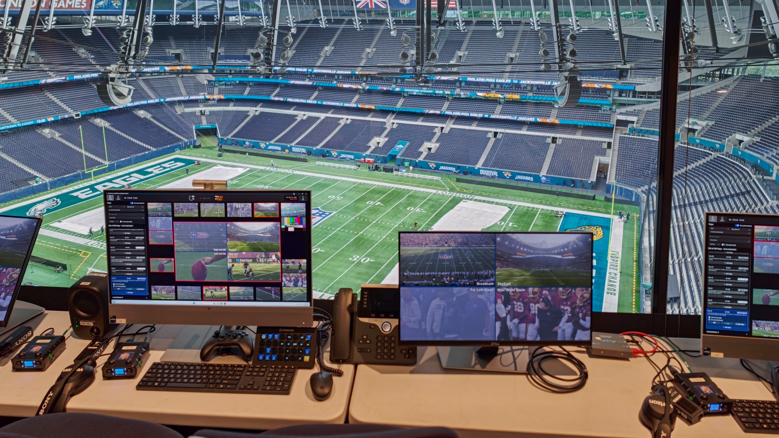 Broadcast control room overlooking the football field, with multiple monitors showing live camera feeds from around the stadium.