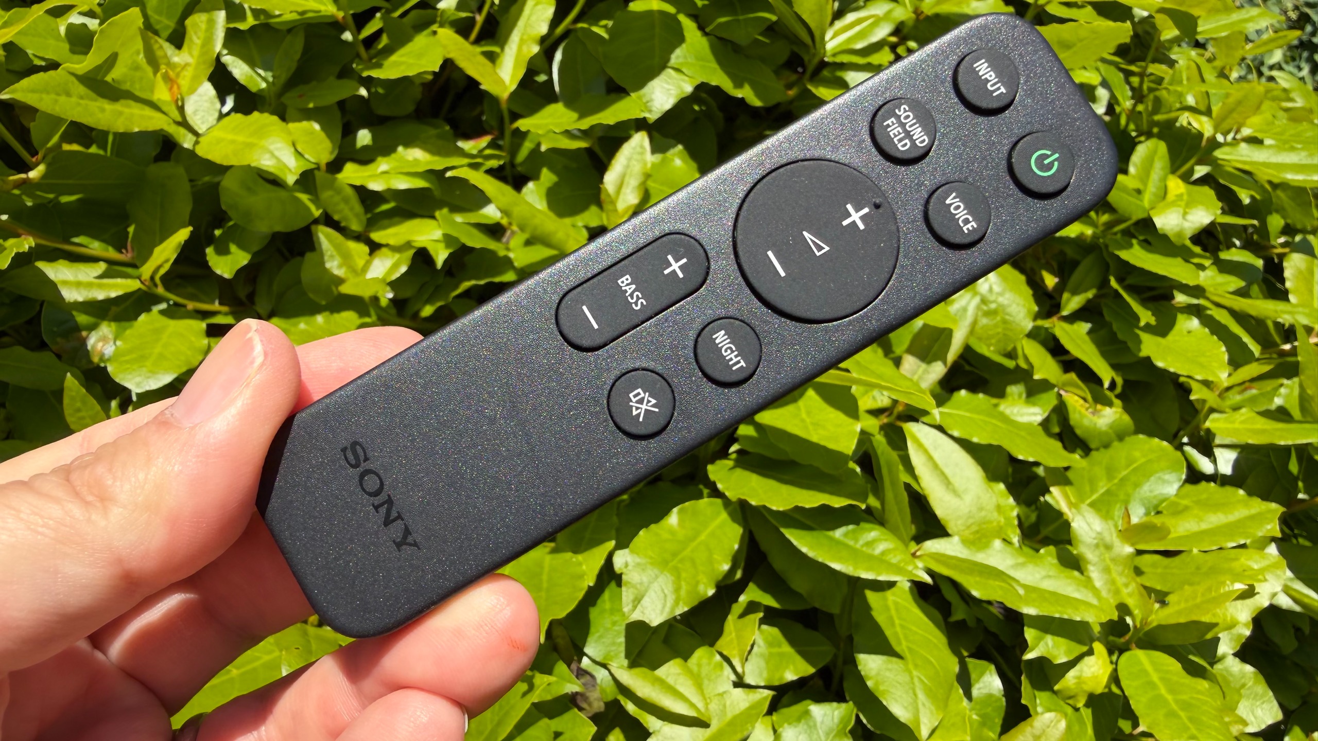 A hand holds the remote for the Sony Bravia Theater Trio.