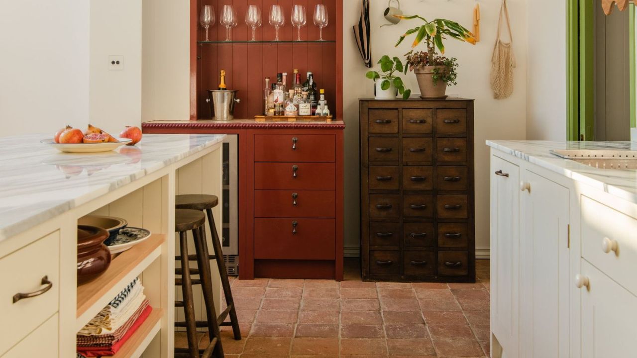 neutral off white kitchen with a marble countertop, terracotta floor tiles, and an unexpected red painting bar cupboard