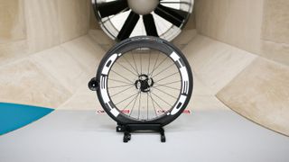 A front HED wheel sits in front of the fan within a wind tunnel