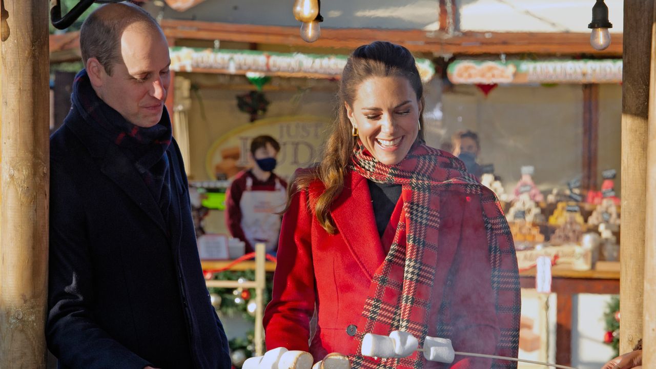 Kate Middleton wearing a red plaid scarf and red coat roasting marshmallows with Prince William outside