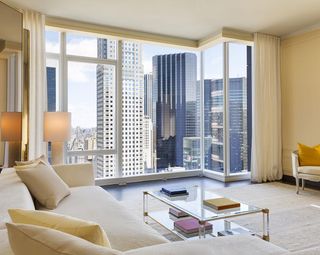A modern hotel room with a white sofa, glass coffee table and a view of the manhattan skyline