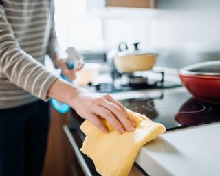 Woman cleaning kitchen counter with yellow cloth