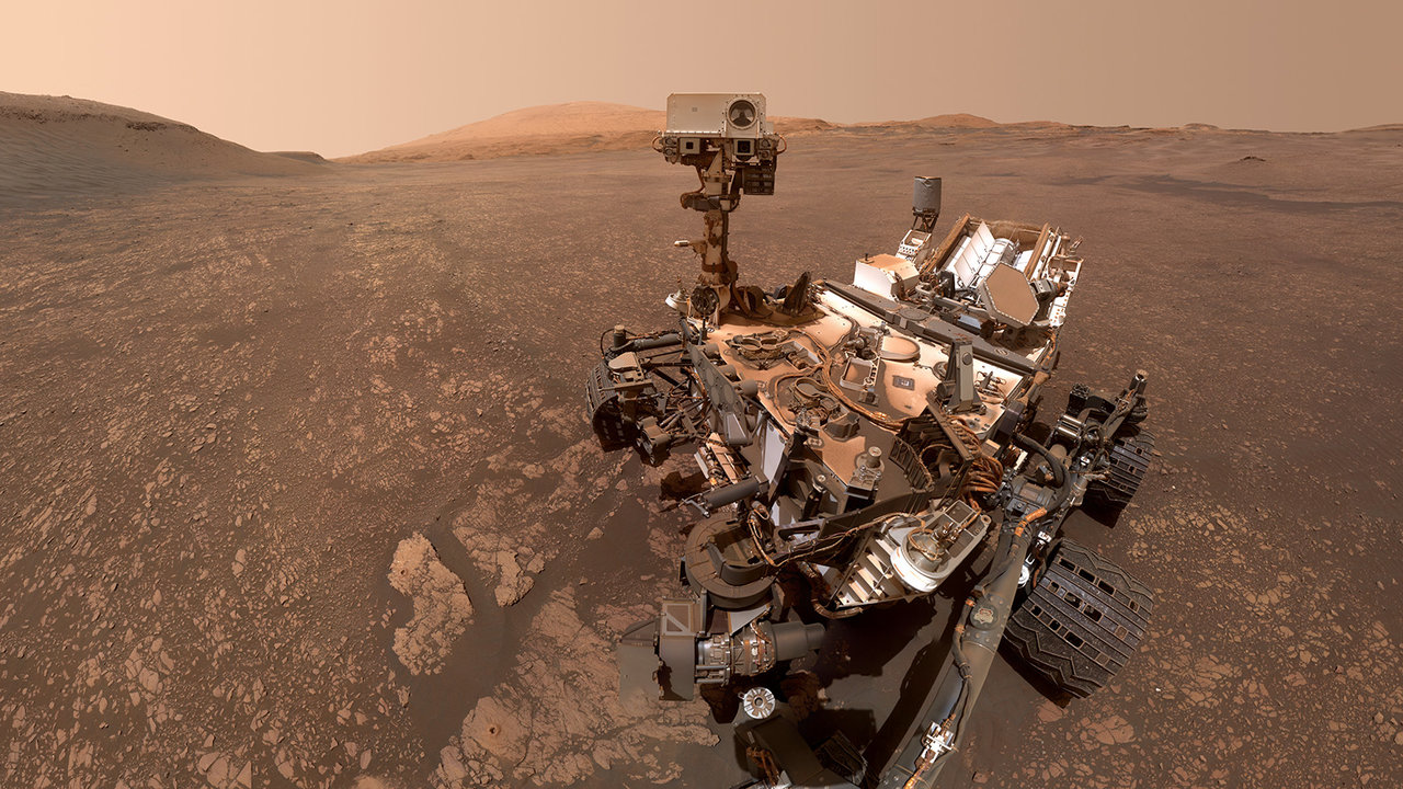 the curiosity rover in front of mars sands and a pale sky