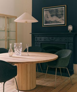 A living room with a dark blue wall and fireplace, a circular wooden dining table and a white light fixture