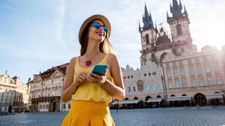 Young woman in yellow walking with smart phone on the old town square in Prague city