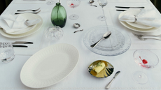 a table with white tablecloth with dinnerware and green velvet curtain behind and vase of flowers