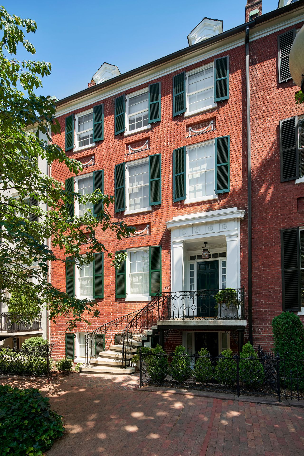 Federal style historic redbrick home exterior with green painted shutters and blue skies with mature trees