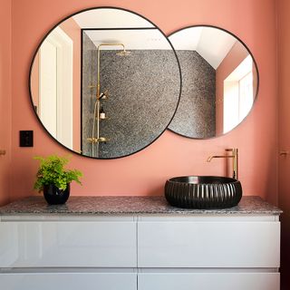 bathroom painted in peach with large wall mirror and black basin