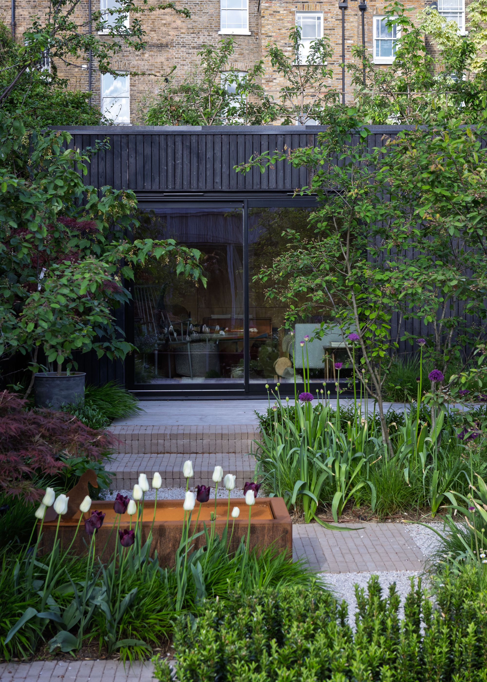 A zoned garden with water feature as a partition in the middle as well as lots of plants in different areas of the space