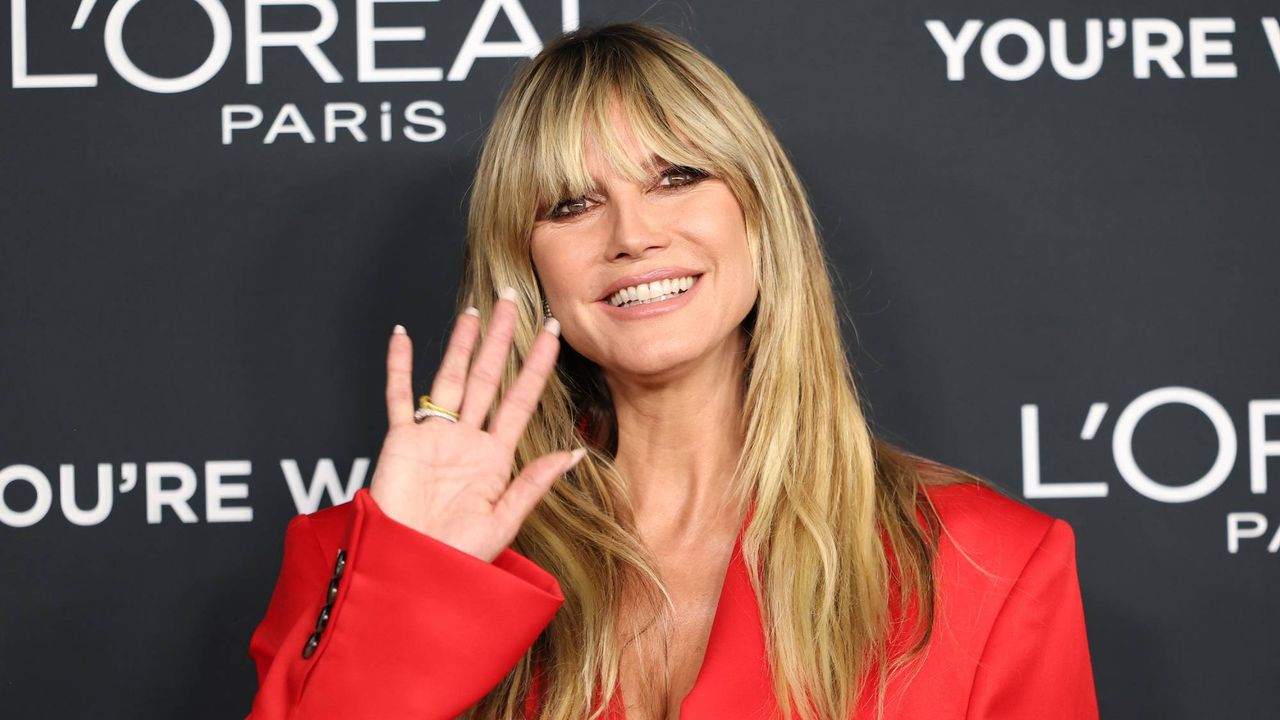 Heidi Klum in a red suit waving to the camera