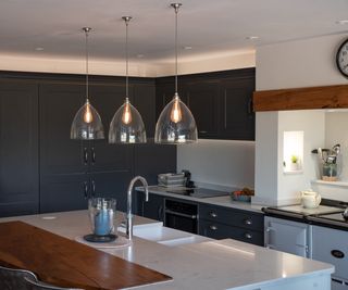 three glass pendant shades hanging above kitchen island with inset sink, tap in kitchen fitted with dark grey units and pale blue Aga cooker