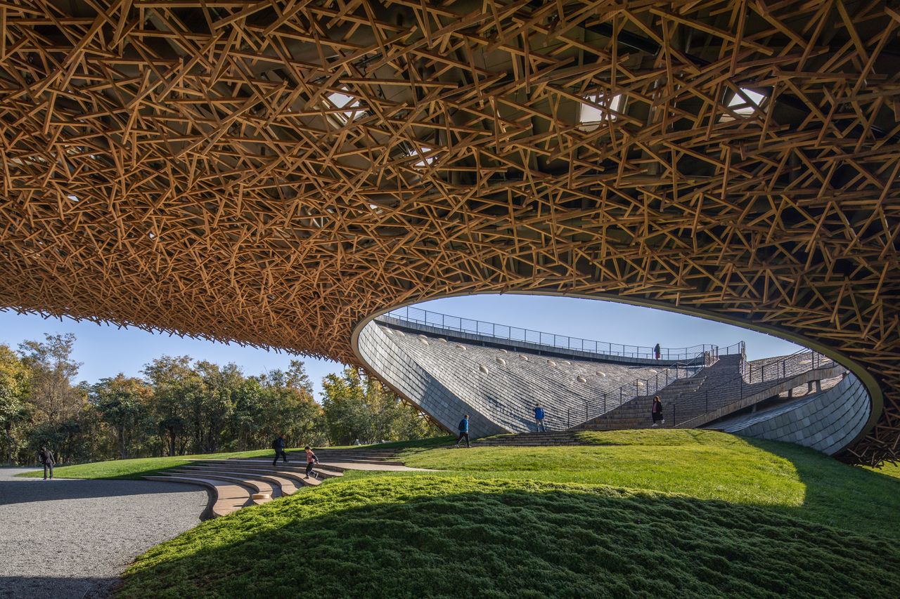 Looking up at the impressive timber roof at Yang liping Performing Arts Center with greenery below and stairs leading to the upper level. 