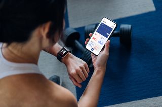 How to workout at home: Over the shoulder view of young active woman using exercise tracking app on smartphone to monitor her training progress after exercising at home