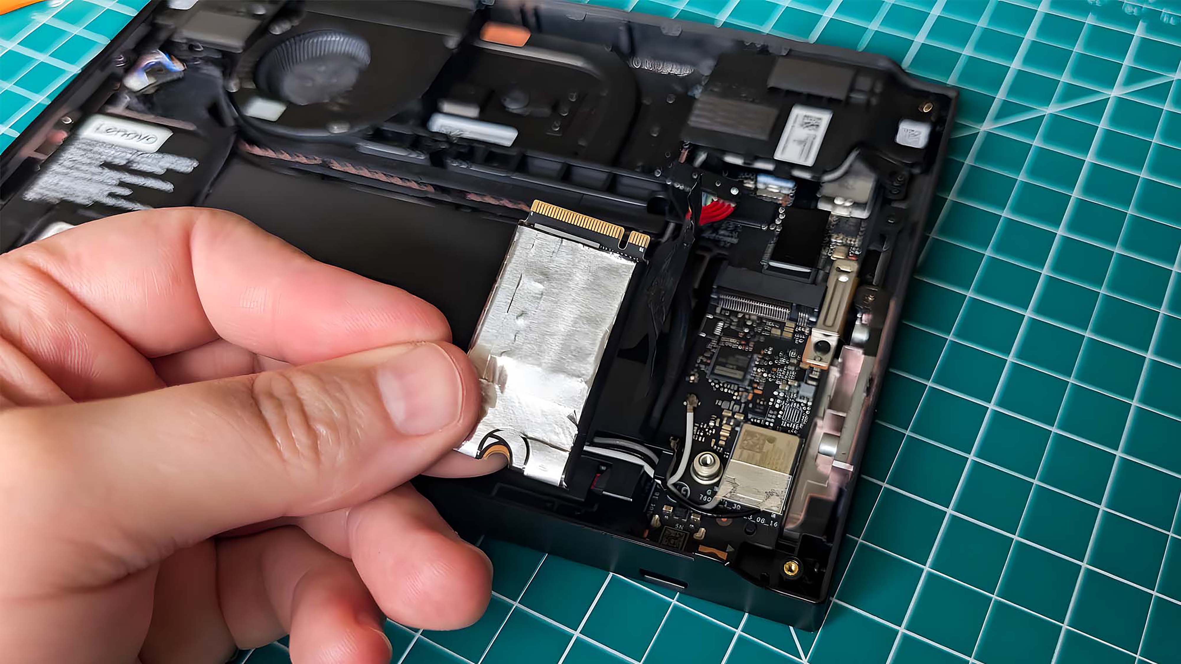 A hand holding the original Lenovo Legion Go SSD over the handheld.