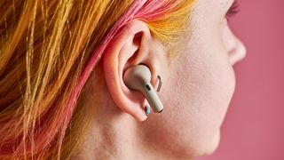 A close up side profile of a woman with orange and pink hair, she has one of the Motorola Moto Plus earbuds in her ear.