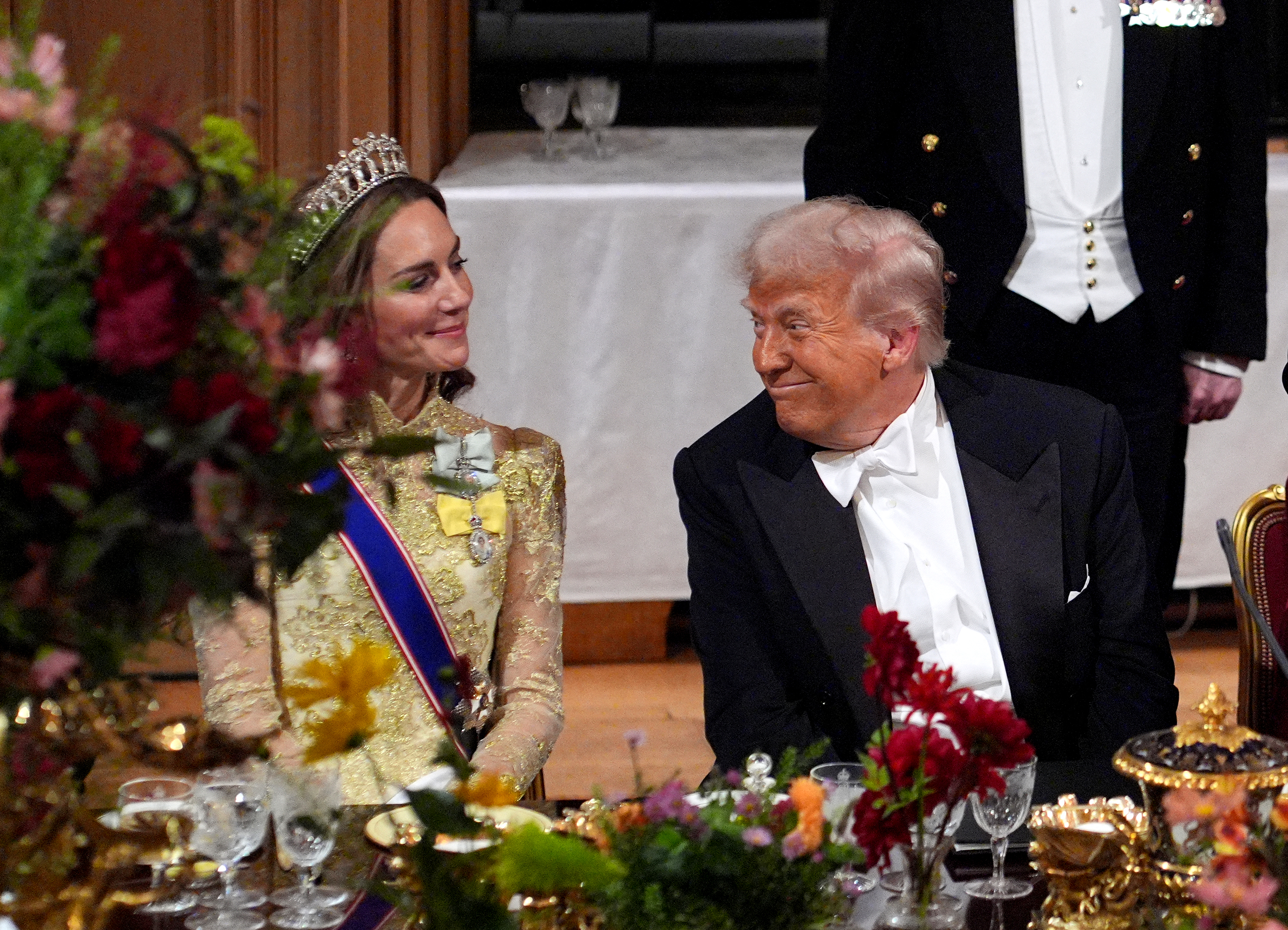 Kate Middleton wearing a gold gown smiling at Donald Trump wearing a tuxedo