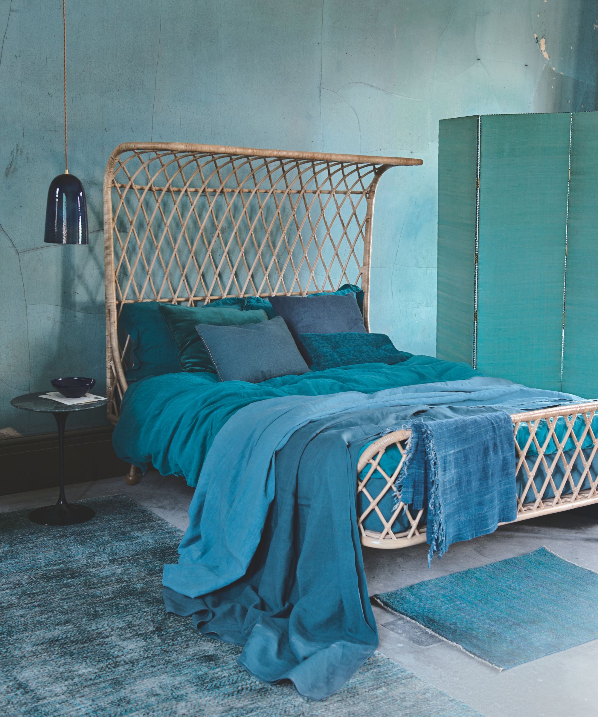 A blue bedroom with blue walls, rattan bed, blue blankets, a blue screen and two blue rugs.
