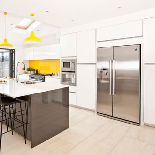 White kitchen with double silver American fridge freezer, island and yellow pendant lights