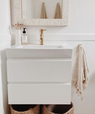 A white bathroom with a sink, mirror, towel, and baskets
