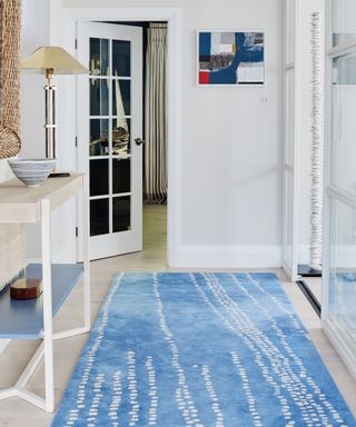 Hallway with pale wooden flooring, blue and white rug and white walls.