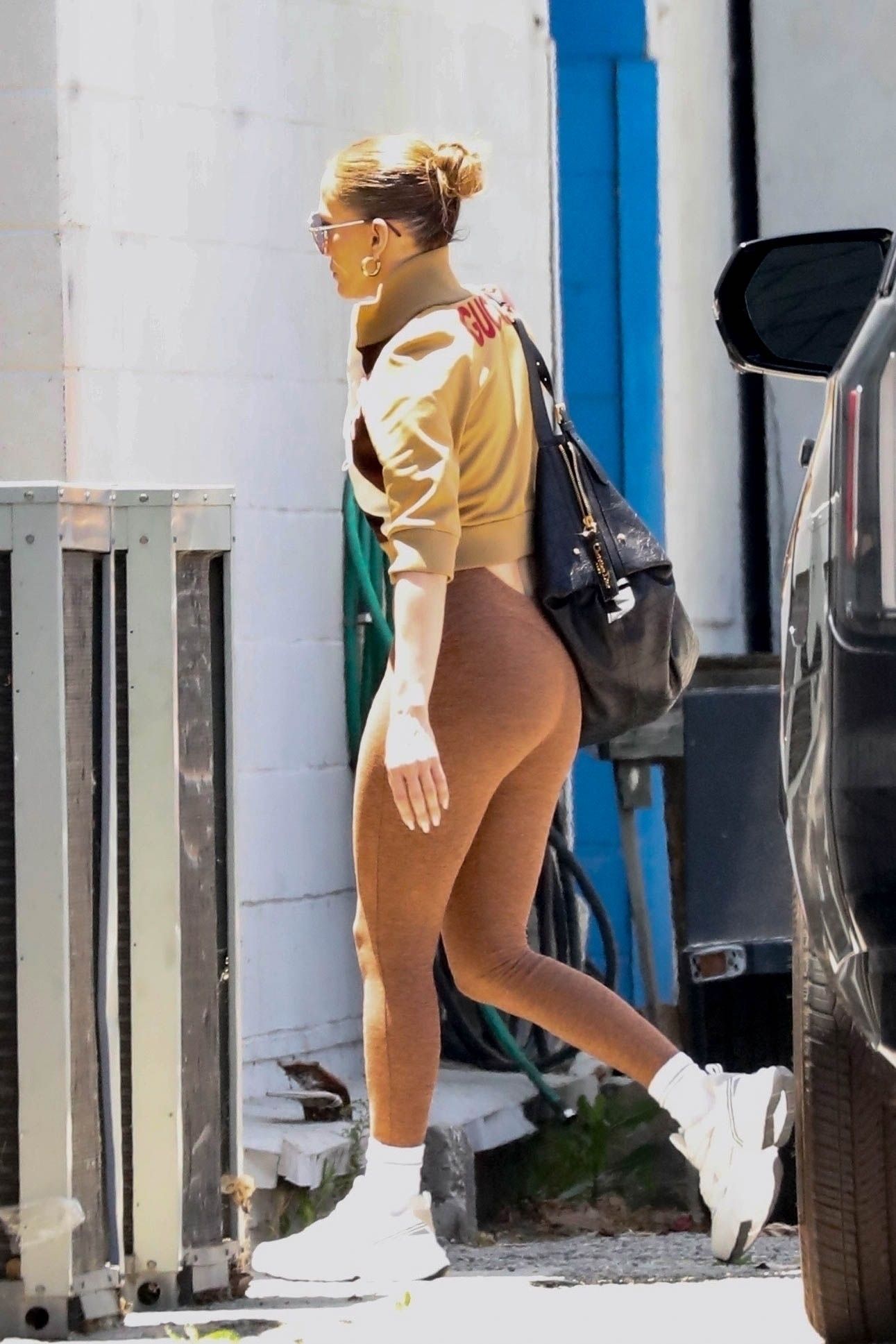 Jennifer Lopez wearing a tan jacket, brown leggings, and white sneakers