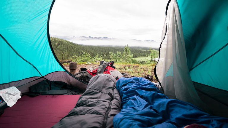 best lightweight sleeping bag: Tent with flap open overlooking forest and two lightweight sleeping bags inside