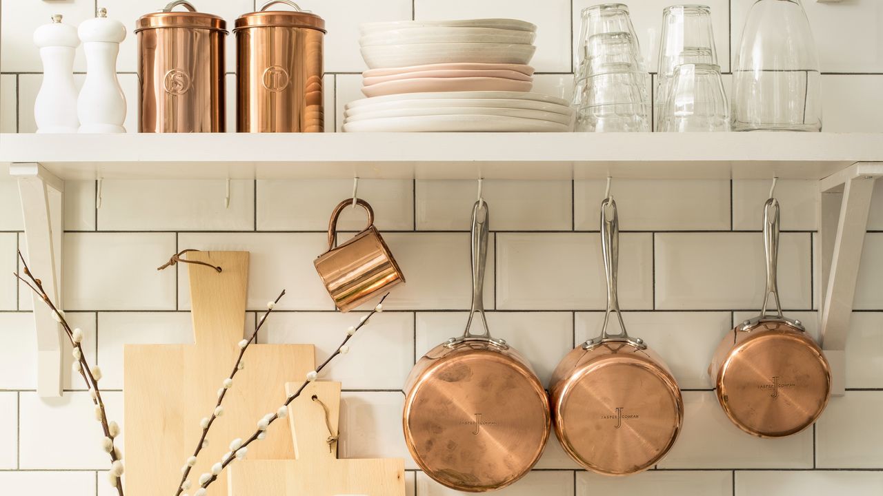 A white-tiled kitchen with hanging copper pots and mug