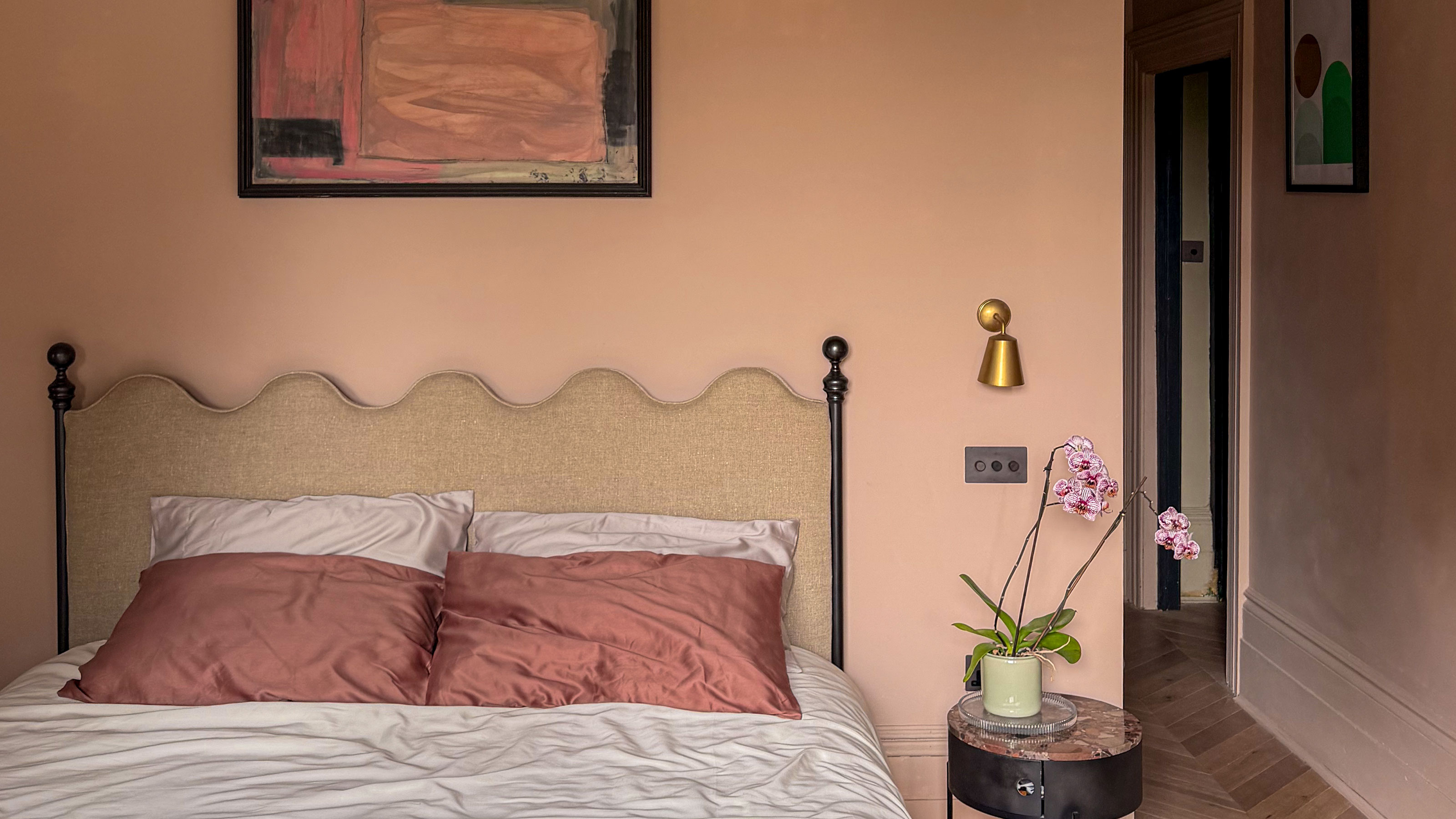 Peach bedroom with wavy headboard, abstract art above bed, and small round bedside table with orchid